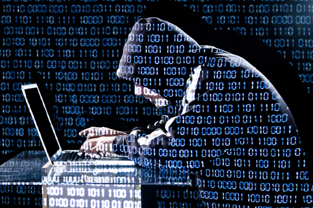 A person in a hoodie using a laptop with the image overlayed with zeros and ones