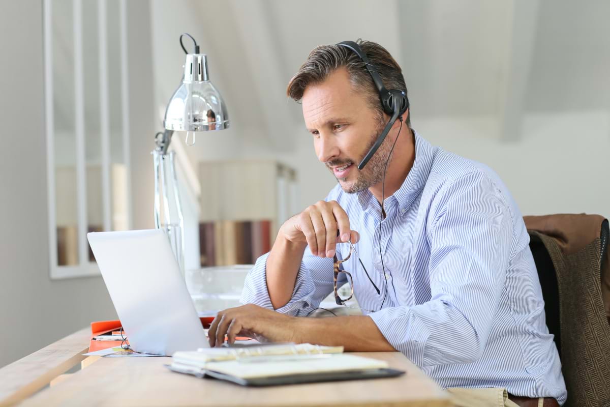 A man wearing a headset working from home on his laptop while taking notes